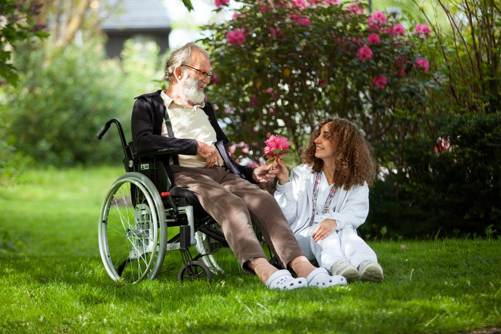 To personer sitter ute en hage. Begge holder på en rosa blomst og smiler.