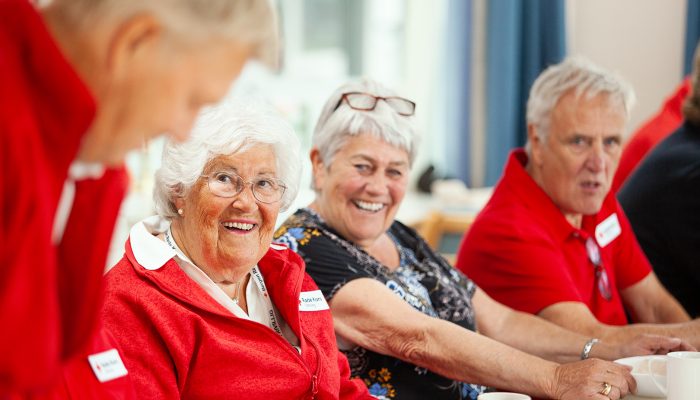 Tre frivillige arbeidere ved Bergen Røde Kors Sykehjem som sitter ved et bord med kaffekopper.