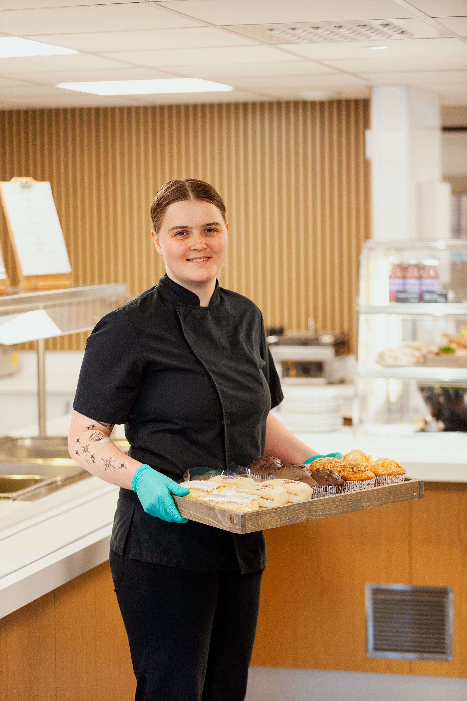 Person som holder et brett med muffins og ulike kaker.