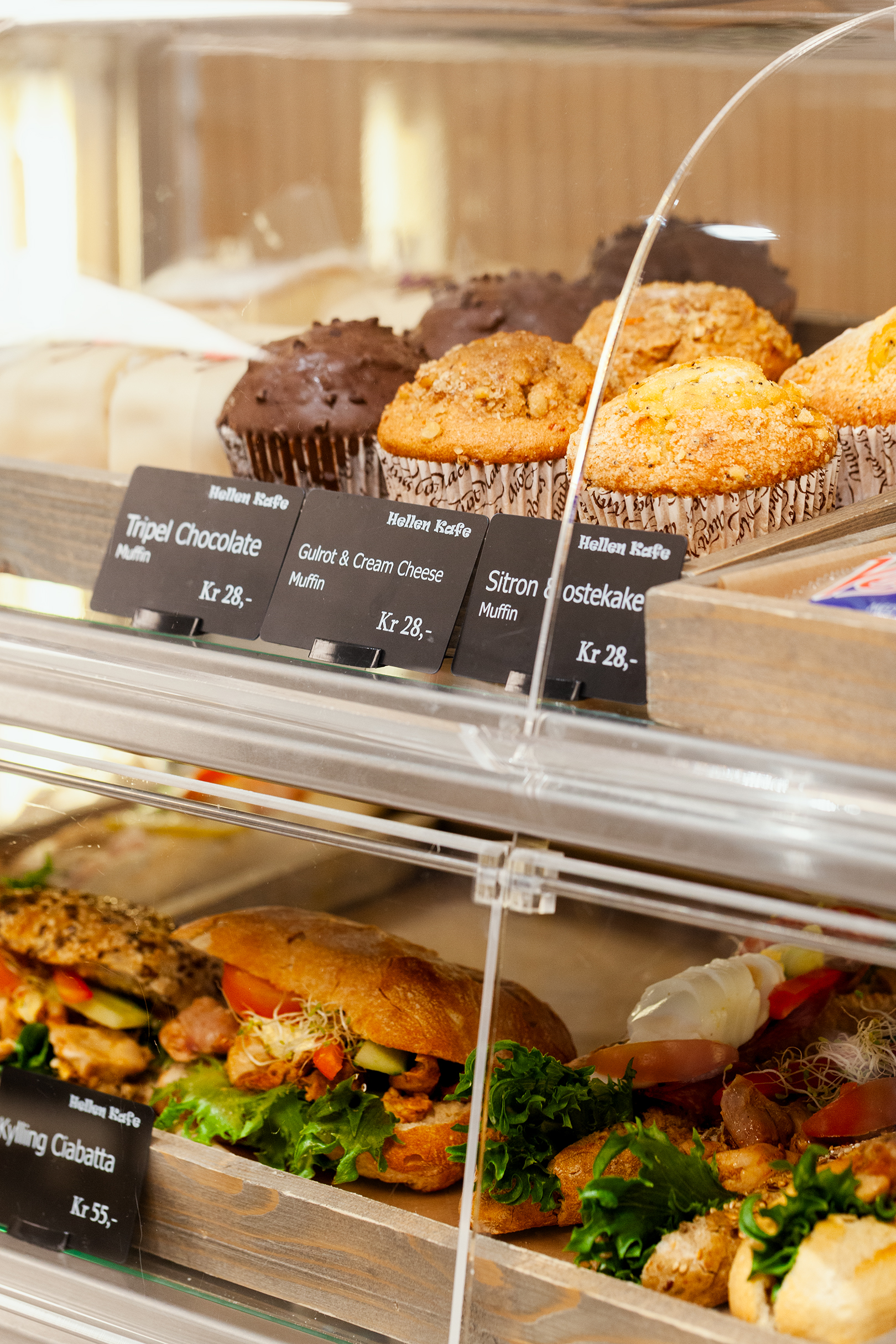 Muffins og ciabetta rundstykker som ligger i brett bak et glasspanel.