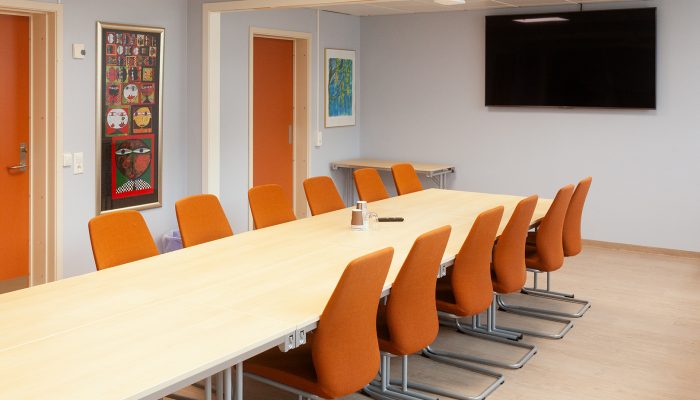Et sett med stoler som er satte ved et langt møteromsbord. TV i bakgrunnen.