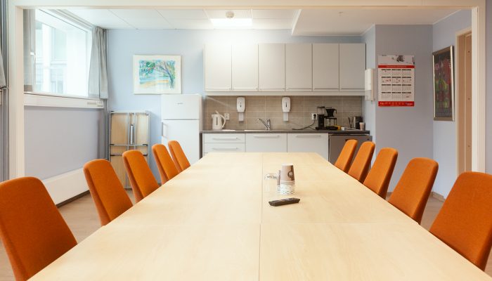 Et sett med stoler som er satte ved et langt møteromsbord. Kjøkken i bakgrunnen.