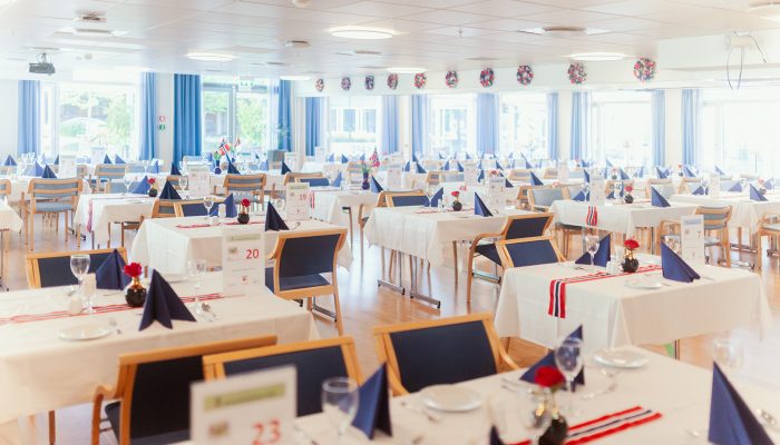 Flere bord som er pådekket med fat, glass og bestikk. Bordene har en hvit duk og dekorbånd på seg.